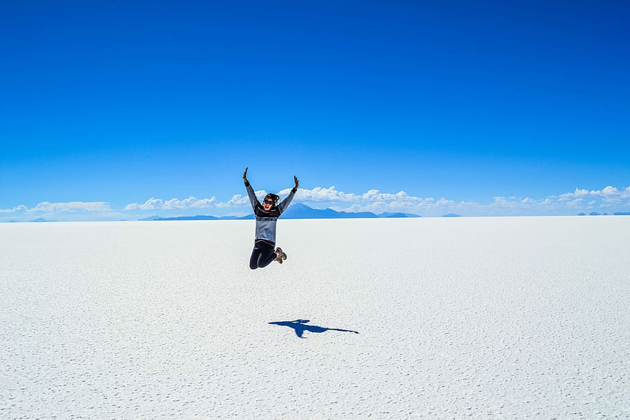 man in black and gray crew-neck sweater jumping under blue sky during daytime HD wallpaper