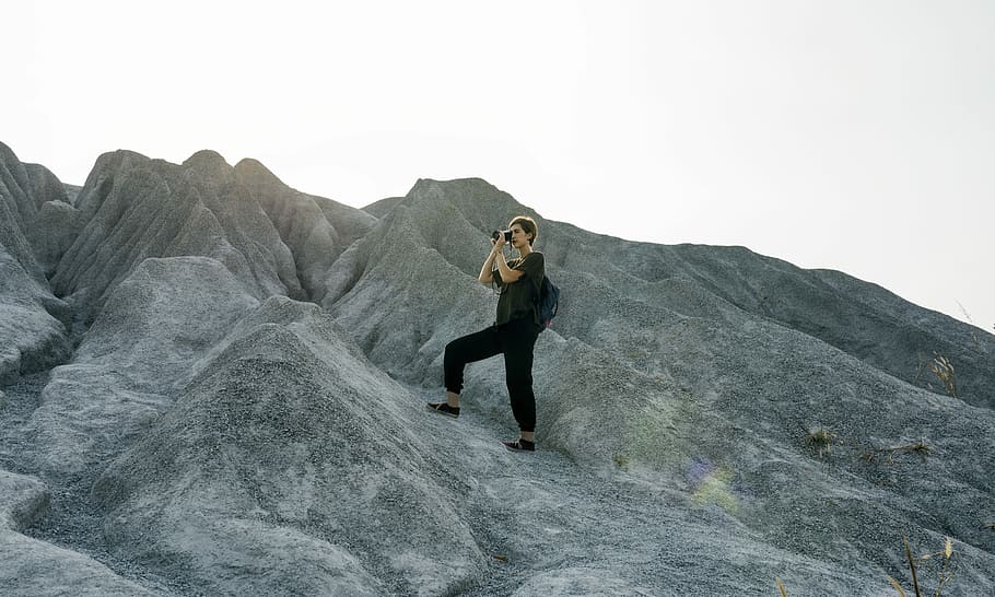 woman carrying black backpack and camera while stepping on rock formation HD wallpaper