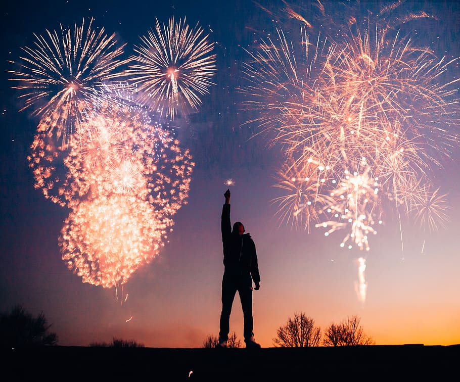 Cause baby you’re a firework, person raising lighted sparkle with fireworks on sky during nighttime HD wallpaper