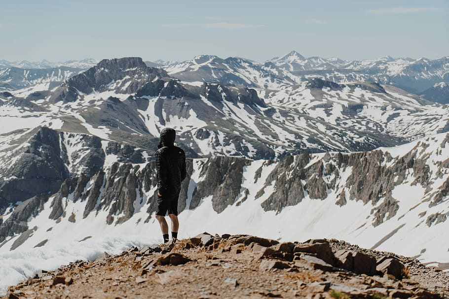 man wearing black shorts standing on rock formation facing on mountain, man standing facing snow coated mountain HD wallpaper