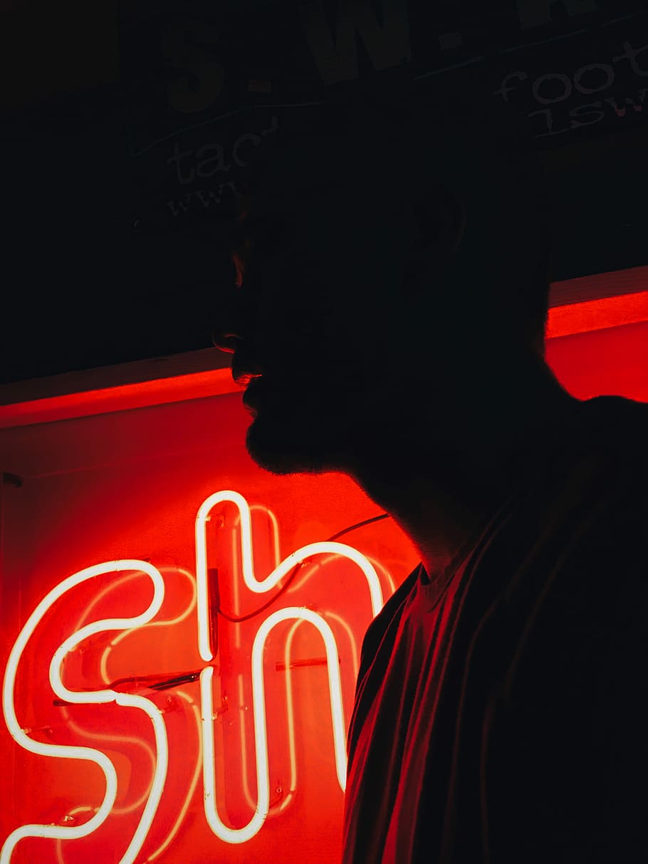 man in front of red SH neon signage, person standing in front of red neon signage