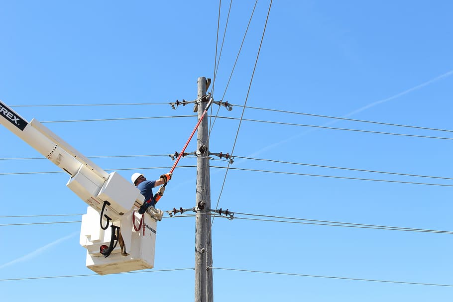 man holding stick near on transmission tower, electrician on crane fixing electric post