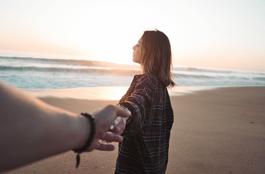 woman holding hands with person facing ocean, woman holding hands on seashore