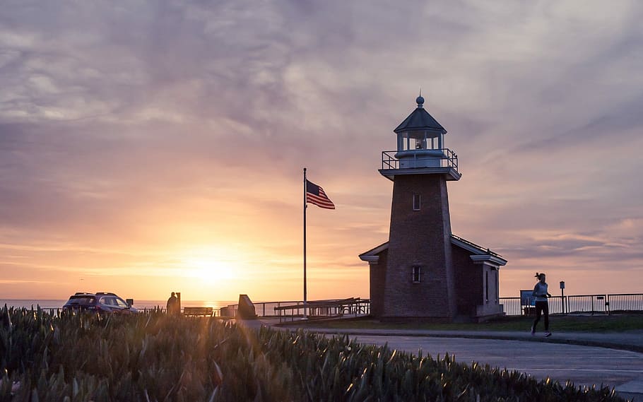 person jogging near lighthouse beside flagpole during sunset, flag of United States of America on pole during golden hour HD wallpaper