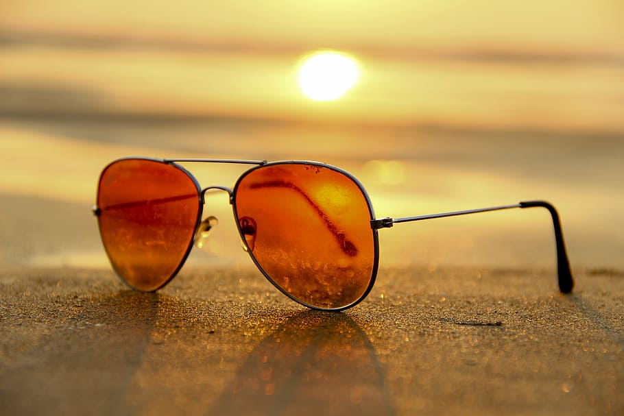 orange aviator sunglasses with silver frames on brown sand, style