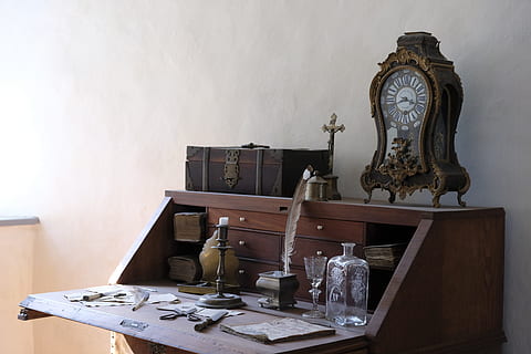 brown wooden analog clock on top of brown wooden slant-top desk near the wall HD wallpaper