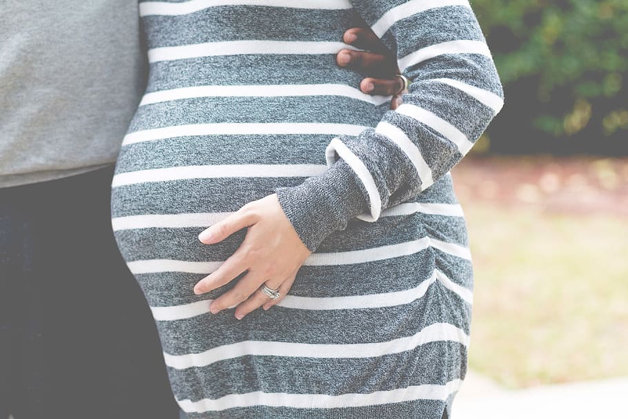 pregnant woman in white and gray striped dress touching her tummy, woman wearing gray and white striped maternity dress