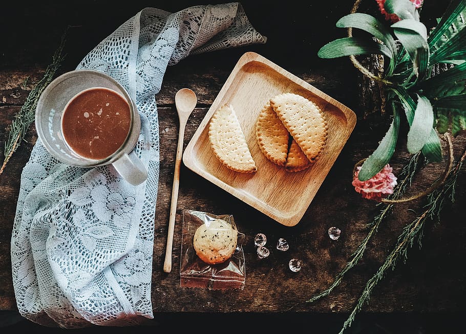 flat-lay photography of pastry on tray beside glass mug, sliced cookies on brown wooden plate beside clear mug on gray lace textile