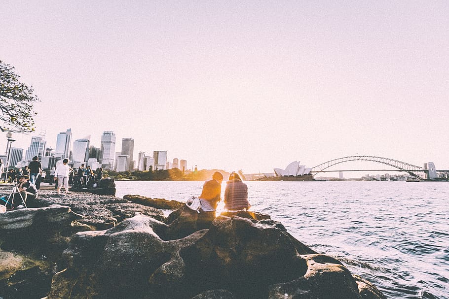 people on shoreline near Sydney opera house and Sydney Harbor bridge during sunset