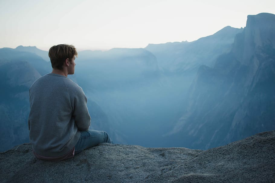 man in gray shirt sits on cliff, man sitting near cliff during daytime HD wallpaper