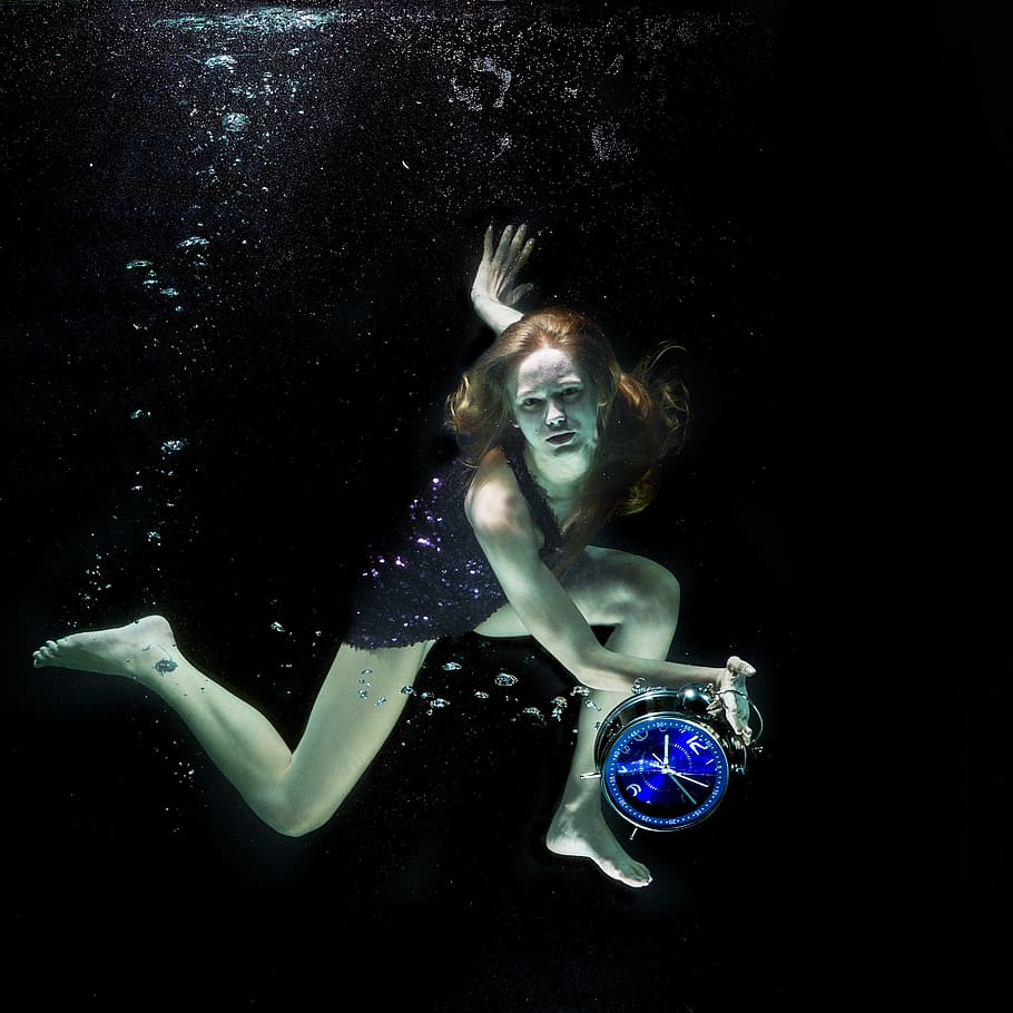 woman wearing black dress holding clock, under water, fashion