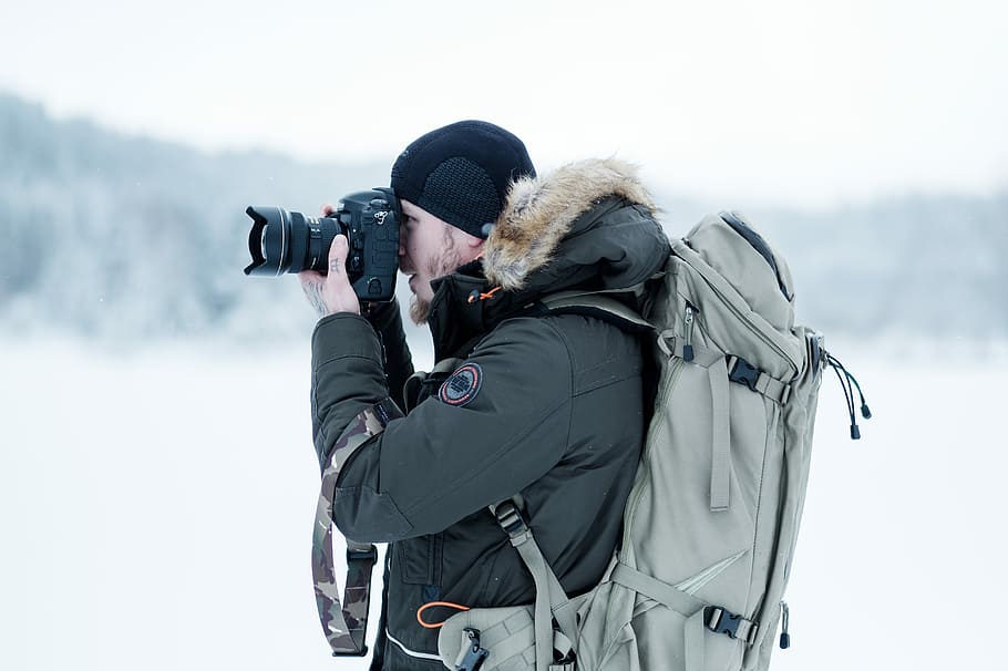 man standing on snow field while taking photo, man in black parka hoodie using smartphone HD wallpaper