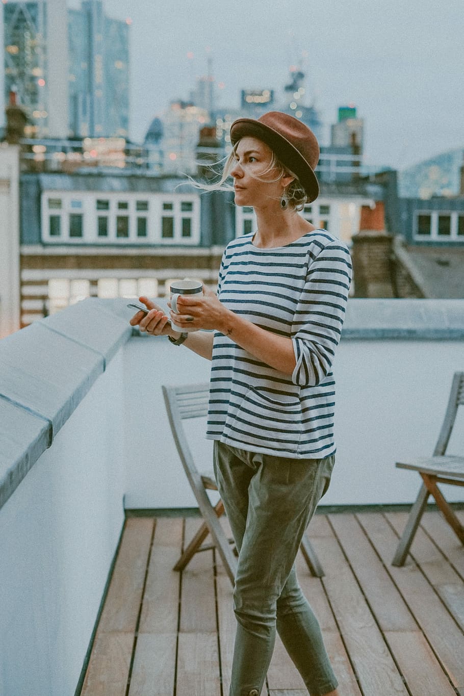 woman in white and black striped shirt holding mug, woman holding mug standing near white wooden chair during daytime HD wallpaper