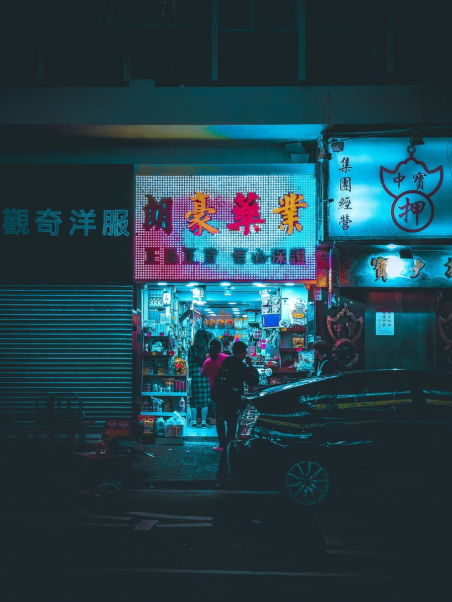 two person standing near storefront during nighttime, person standing in front of gray building