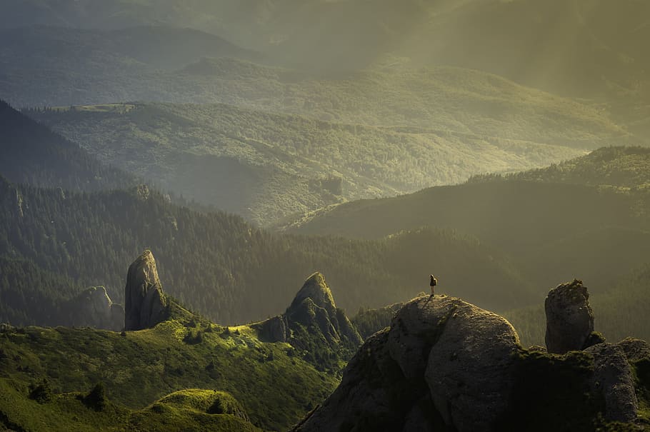 landscape photography of mountain hit by sun rays, person standing on top of rocky mountain at daytime