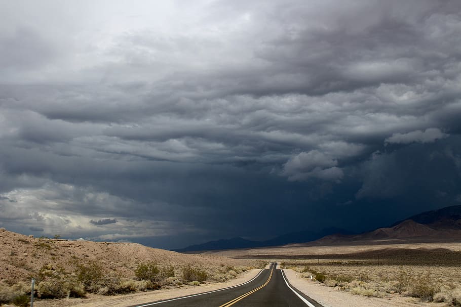 gray asphalt road under blue sky during daytime, asphalt road between desert under dark cloudy sky HD wallpaper