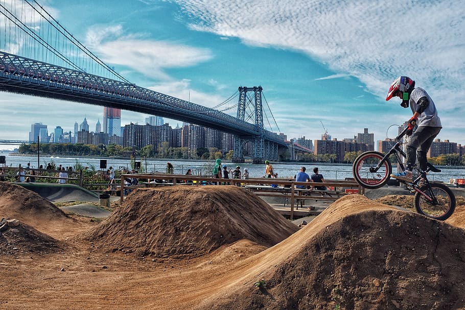 man riding BMX bike on soil ramps near gray bridge during daytime, person riding on black BMX bike during daytime HD wallpaper