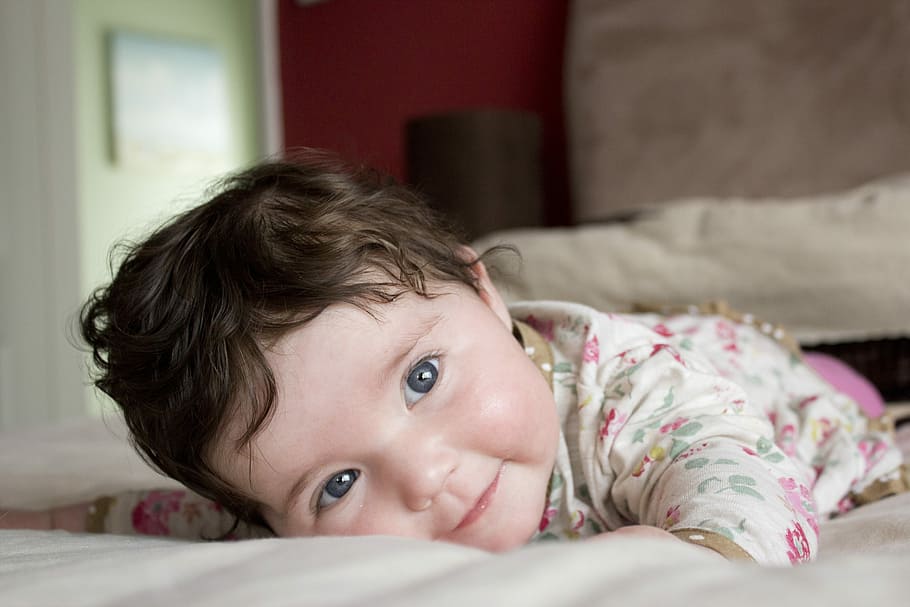 baby girl wearing white and pink top lying on bed, floral, onesie