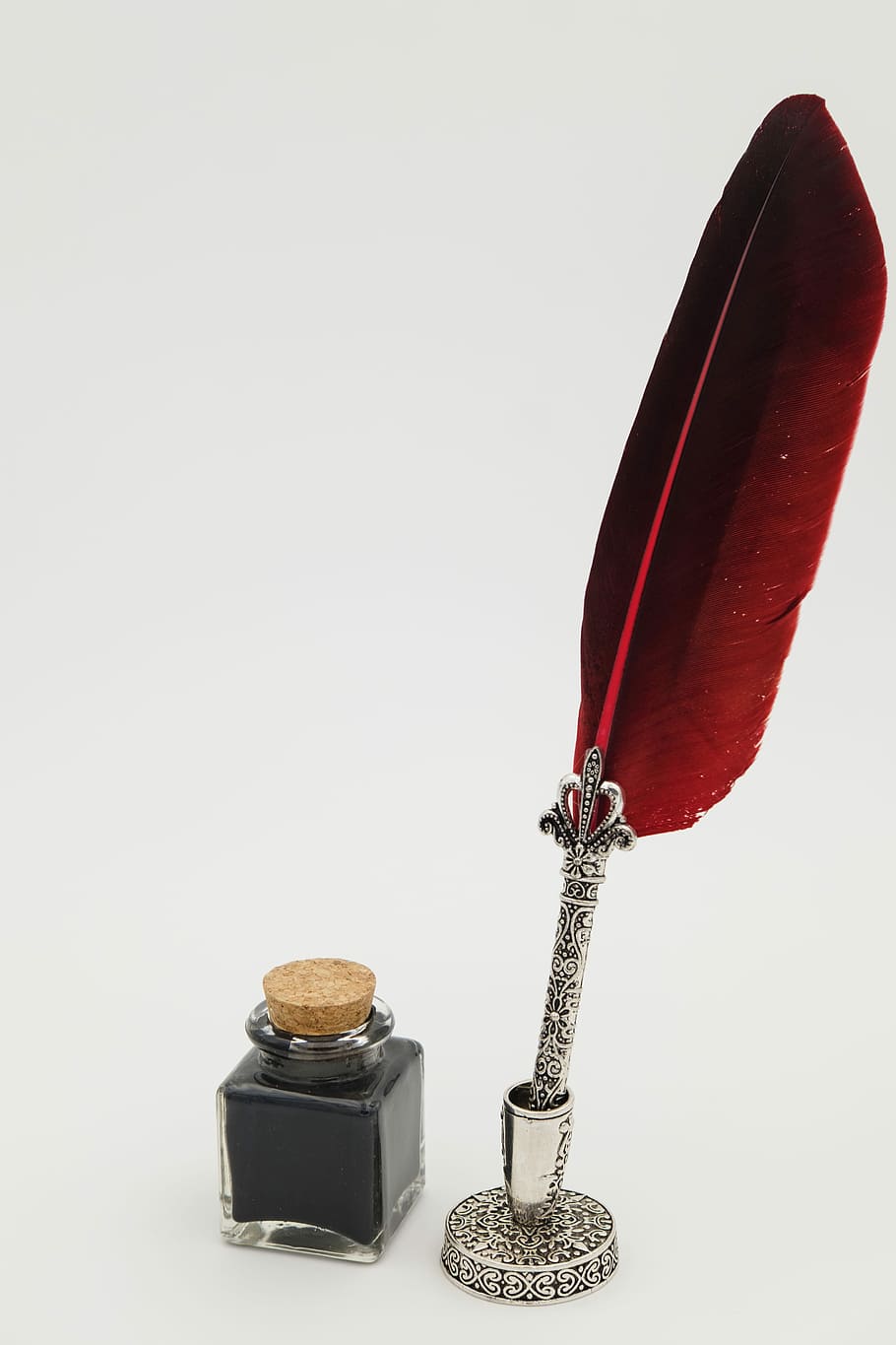 gray and red fountain pen with red feather beside ink bottle
