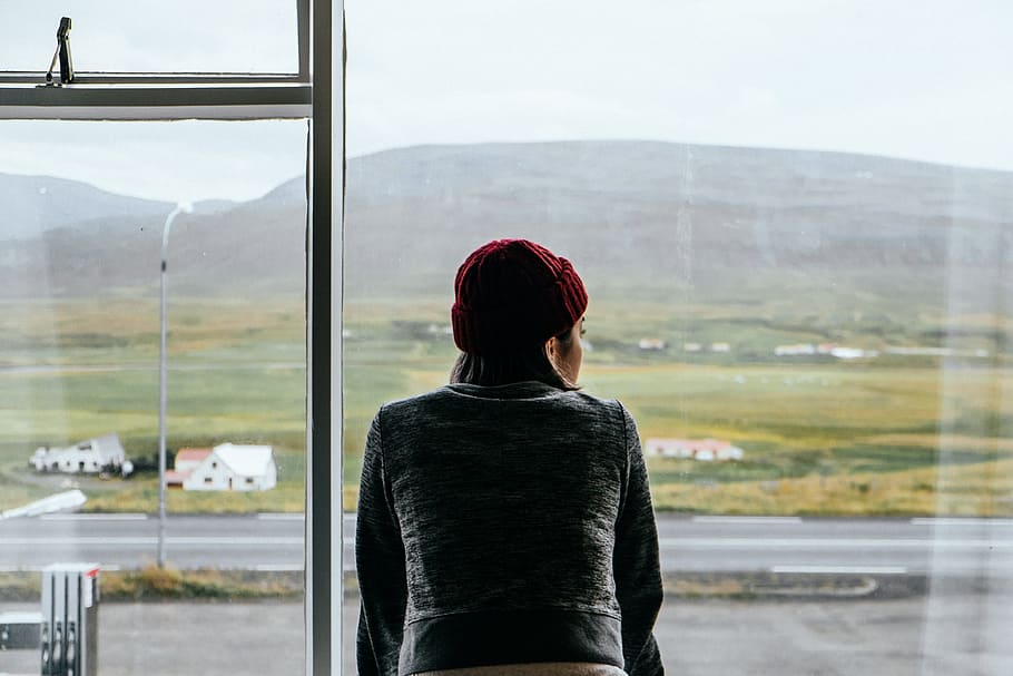 woman standing on glass window, woman wearing gray coat and red knit cap looking at distance over clear glass window HD wallpaper
