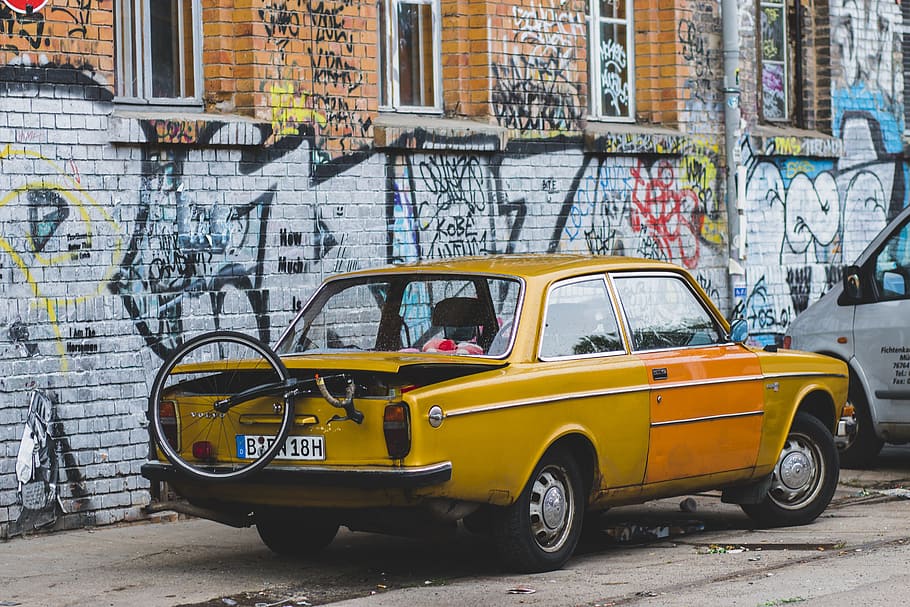 vintage yellow coupe with unicycle on back park near graffiti wall, brown coupe parked near wall with graffiti HD wallpaper