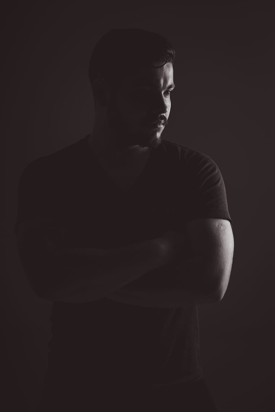 man in black t-shirt standing near black wall, low light photography