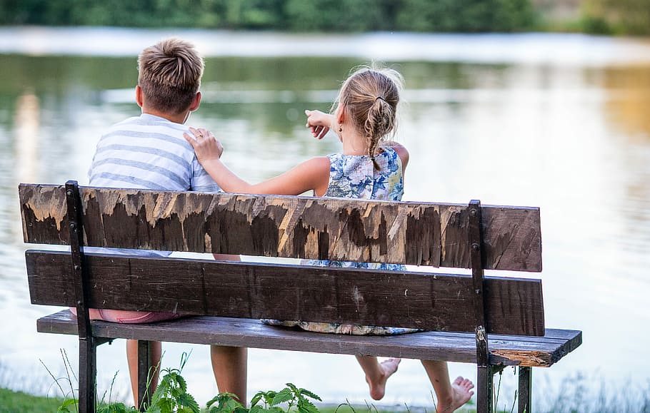 girl and boy sitting on brown wooden bench near body of water at daytime, HD wallpaper