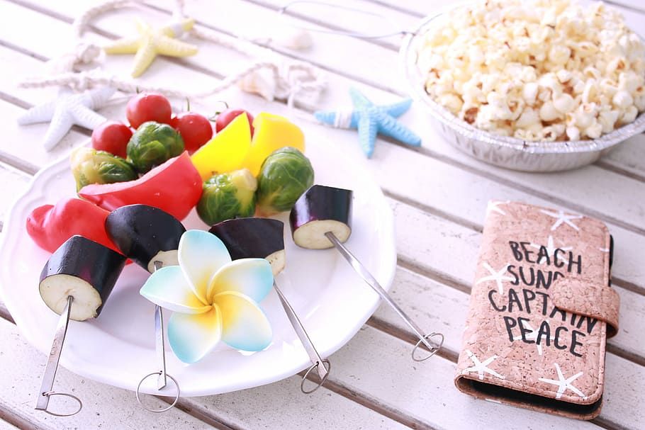 vegetable skewers on round ceramic plate near popcorn and brown leather flip phone case on white wooden surface HD wallpaper