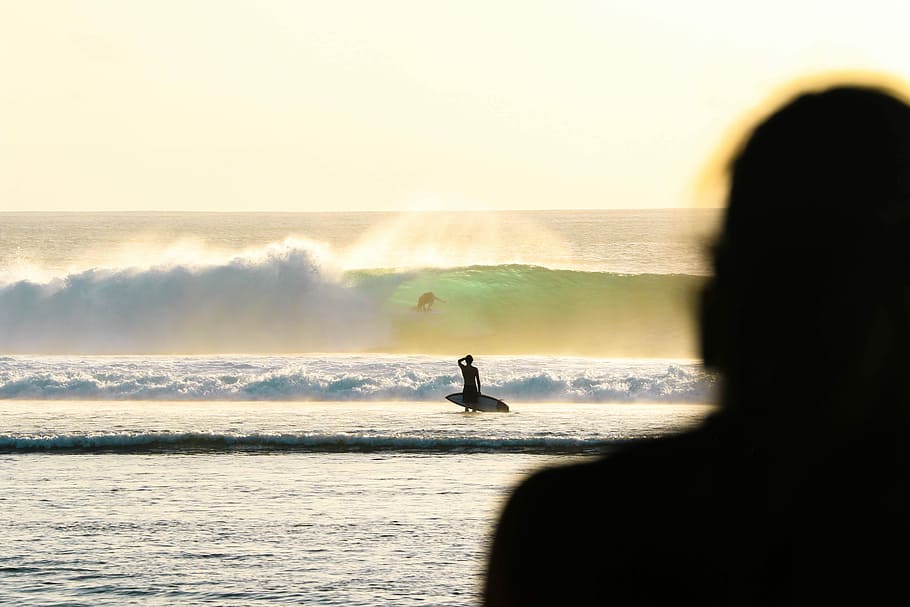 person holding white surfboard, silhouette of man holding surfboard near sea waves during daytime HD wallpaper