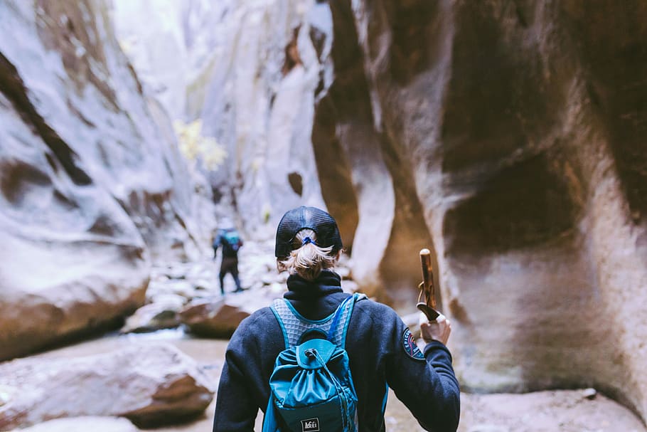two people hiking in the middle of huge rock formations, person wearing backpack beside mountain HD wallpaper