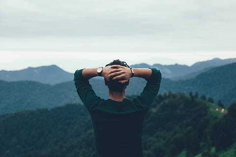man wearing green raglan watching the mountain, man with arms behind his head facing the forest during day HD wallpaper