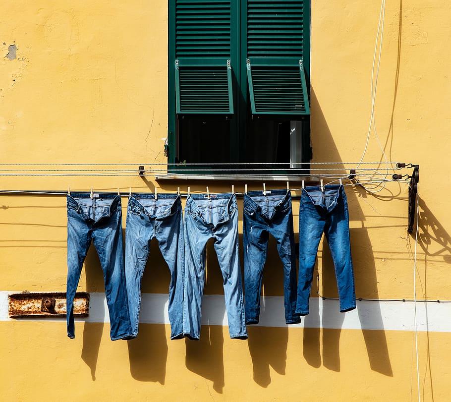 five blue denim jeans hanged on grey cable near window, five blue denim pants hanging