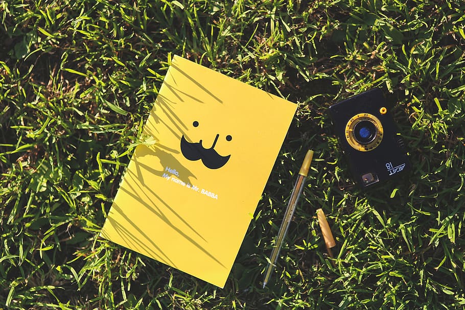 yellow book beside ballpen on green grass, notebook, camera HD wallpaper