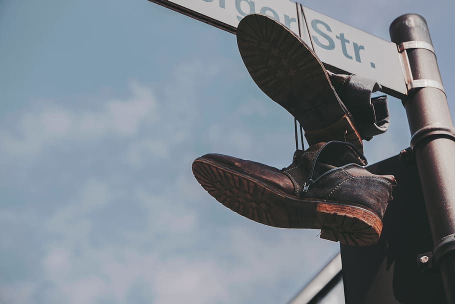 pair of black boots hanged on street post, pair of brown leather shoes hanging on street sign during daytime HD wallpaper