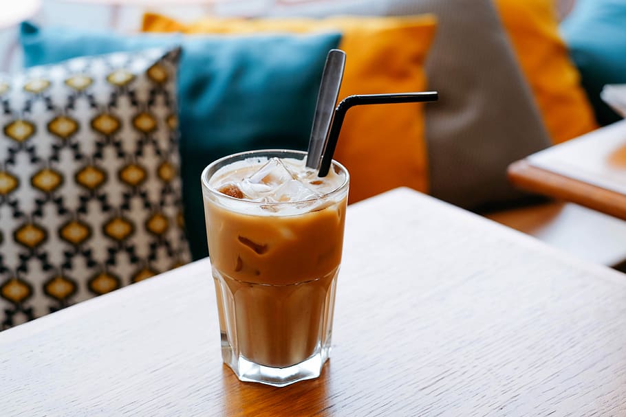 iced juice on table, clear drinking glass filled with iced coffee on brown wooden table