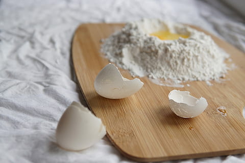 Making pasta, egg shell on brown chopping board beside flour with egg inside HD wallpaper