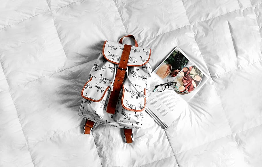 white and brown leather backpack on white textile beside book HD wallpaper