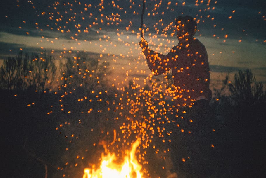 man playing bone fire, man holding a stick in front of a firewood HD wallpaper