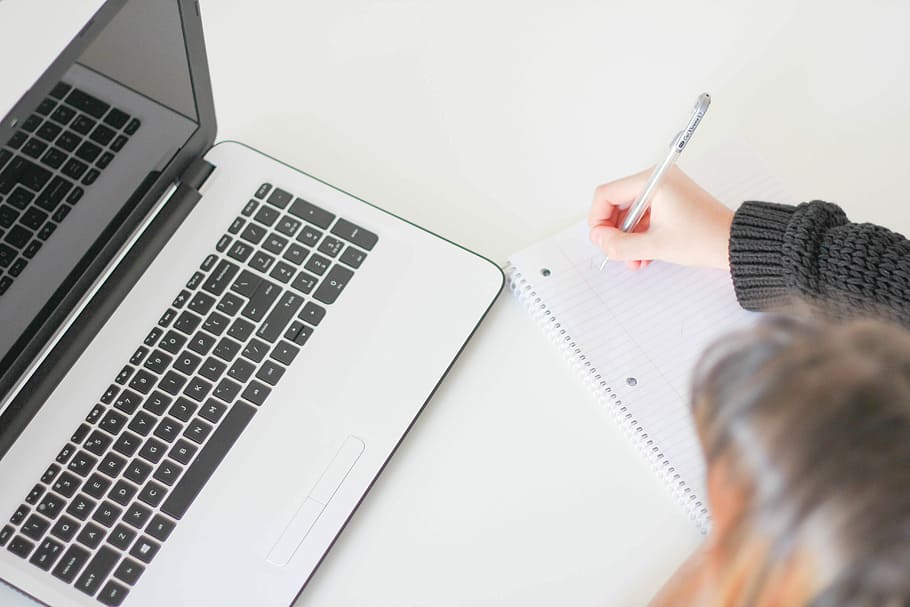 woman writing on notebook, woman writing on white lined paper in front of black and gray laptop computer HD wallpaper