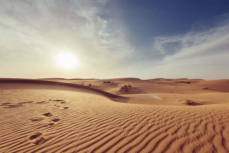 gray sand under white and blue sky, desert with footprints, Sahara desert