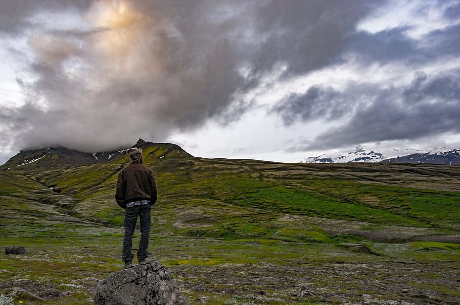 standing man wearing black hoodie on stone under gray sky, adventure HD wallpaper