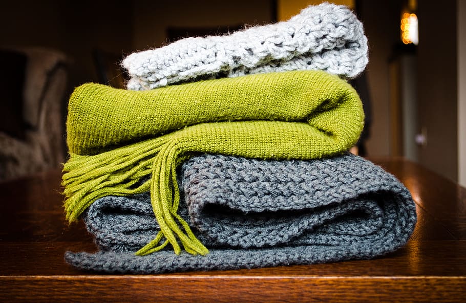 three gray, green, and white scarf on top of table, gray, green, and blue knitted textiles on brown wooden surface