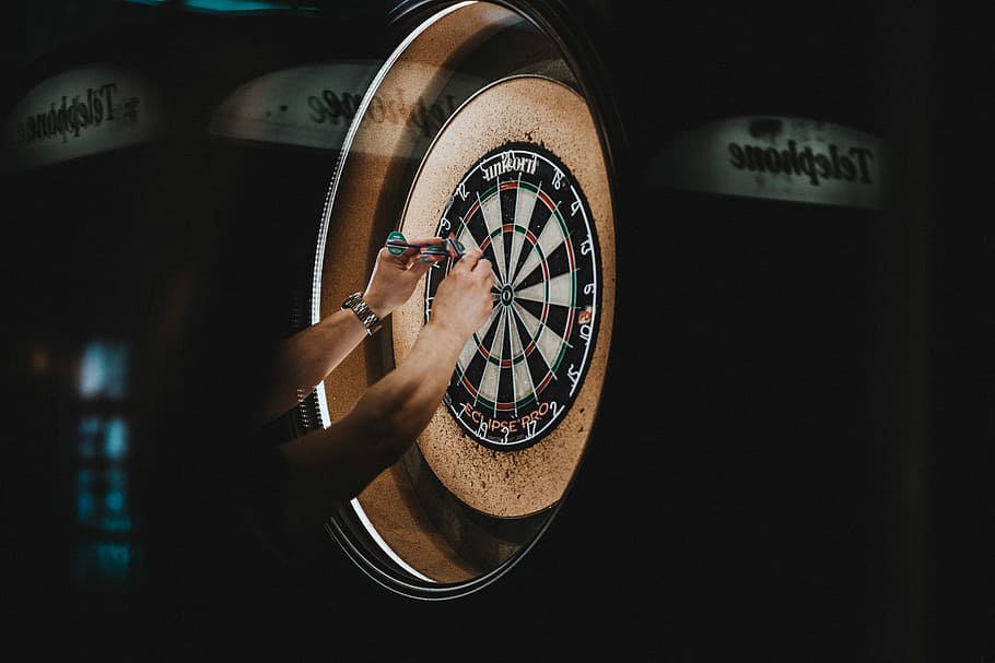 person picking dart pins on board, person removing dart pins on dartboard