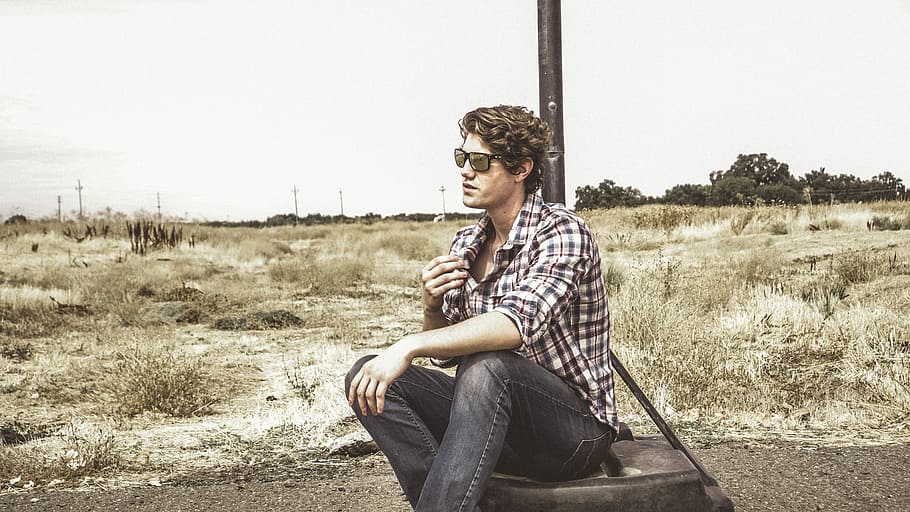 man in white and black plaid sport shirt sitting on tire, person sitting near black pole HD wallpaper