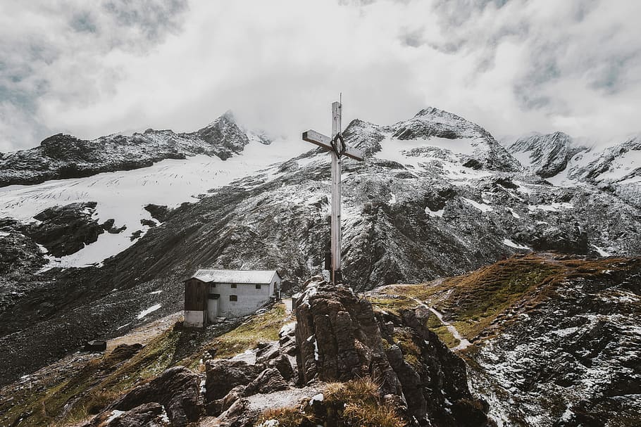 gray cross on top of hill, photo of cross on rocky hill near white concrete building and snow-covered mountain HD wallpaper