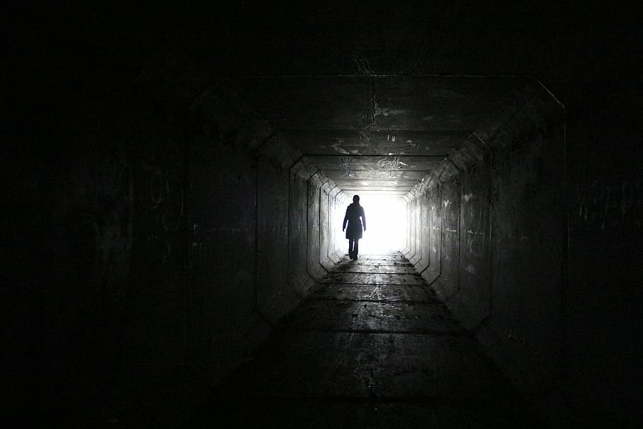 silhouette of a person toward white bright light, outside, tunnel