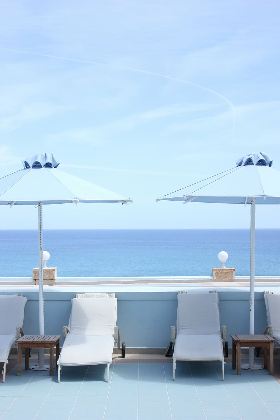 four white outdoor loungers under shade of two blue parasols overlooking sea under clear blue sky during daytime HD wallpaper