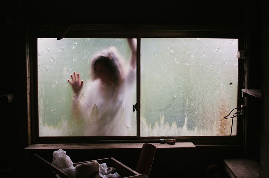 person outside the window, person wearing white shirt leaning on frosted glass window view from dim-lighted room