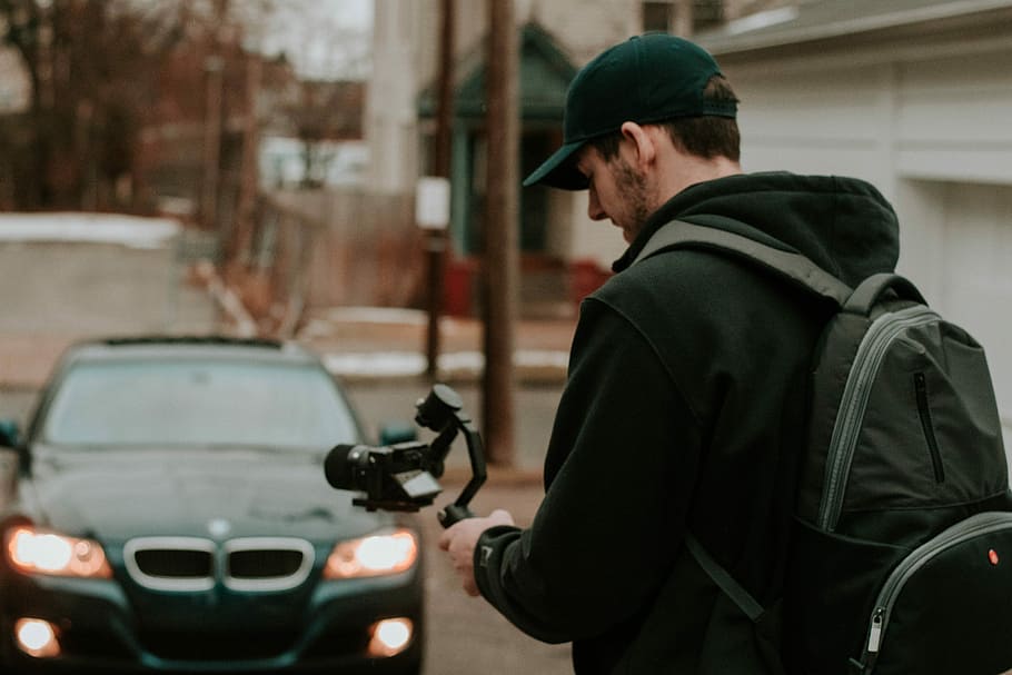 man holding camera in front black BMW car, man standing while holding camera stabilizer HD wallpaper