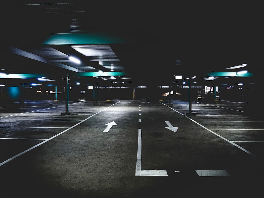 gray concrete parking area under blue building, empty pathway under turned on lights during nighttime